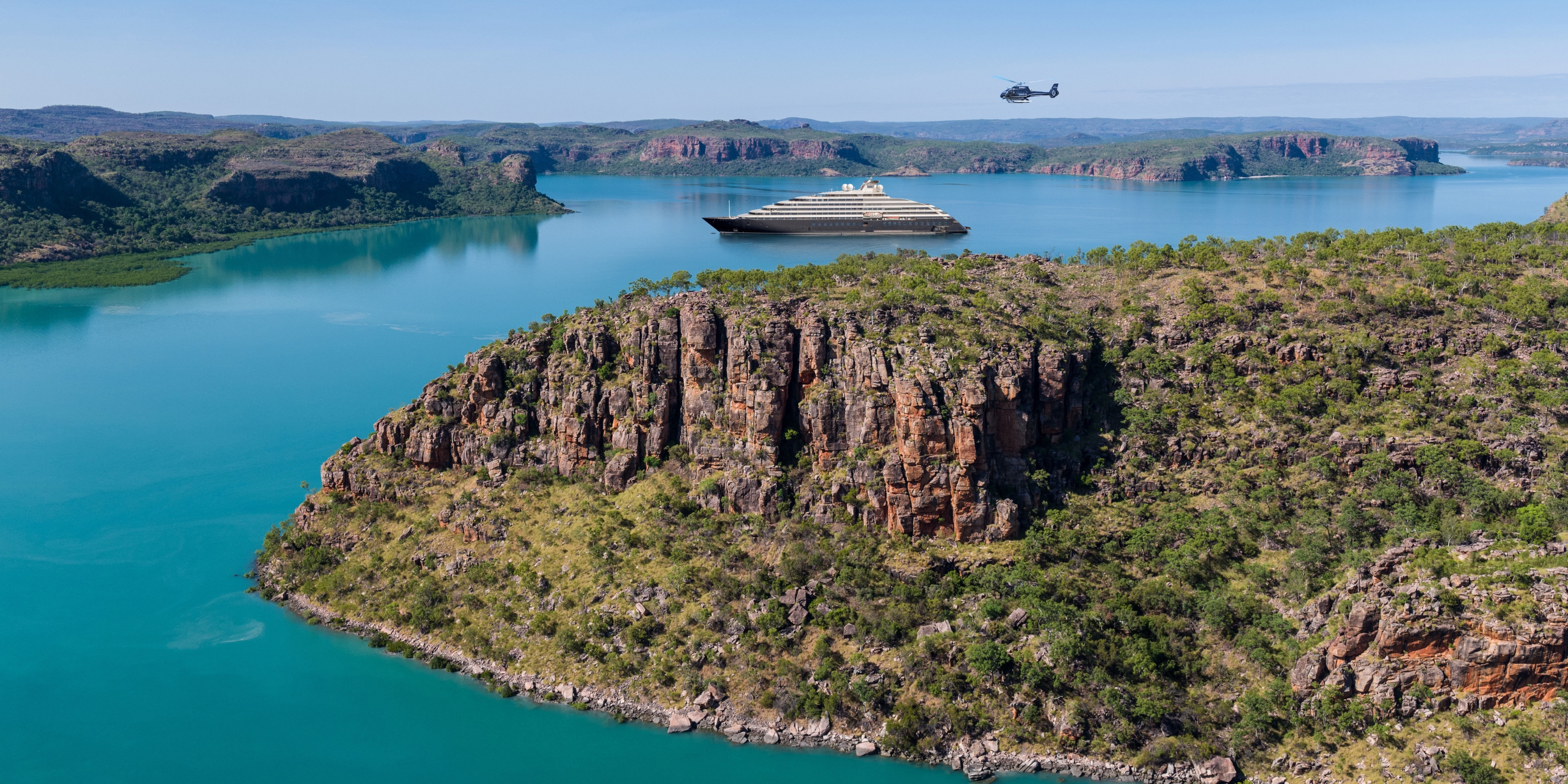 luxury ocean cruise discovery yacht sailing in the blue waters of the kimberleys in Australia with a helicopter flying over head