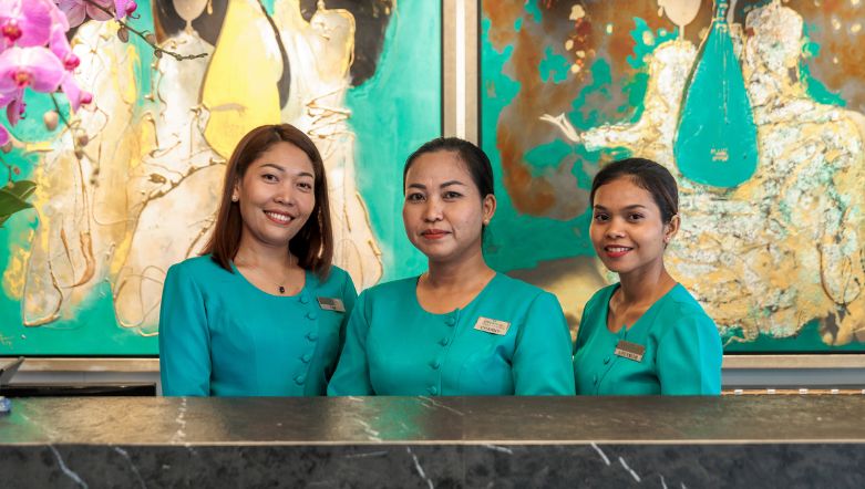 Three ladies standing behind a desk infront of vibrant artwork wearing bright teal tops.