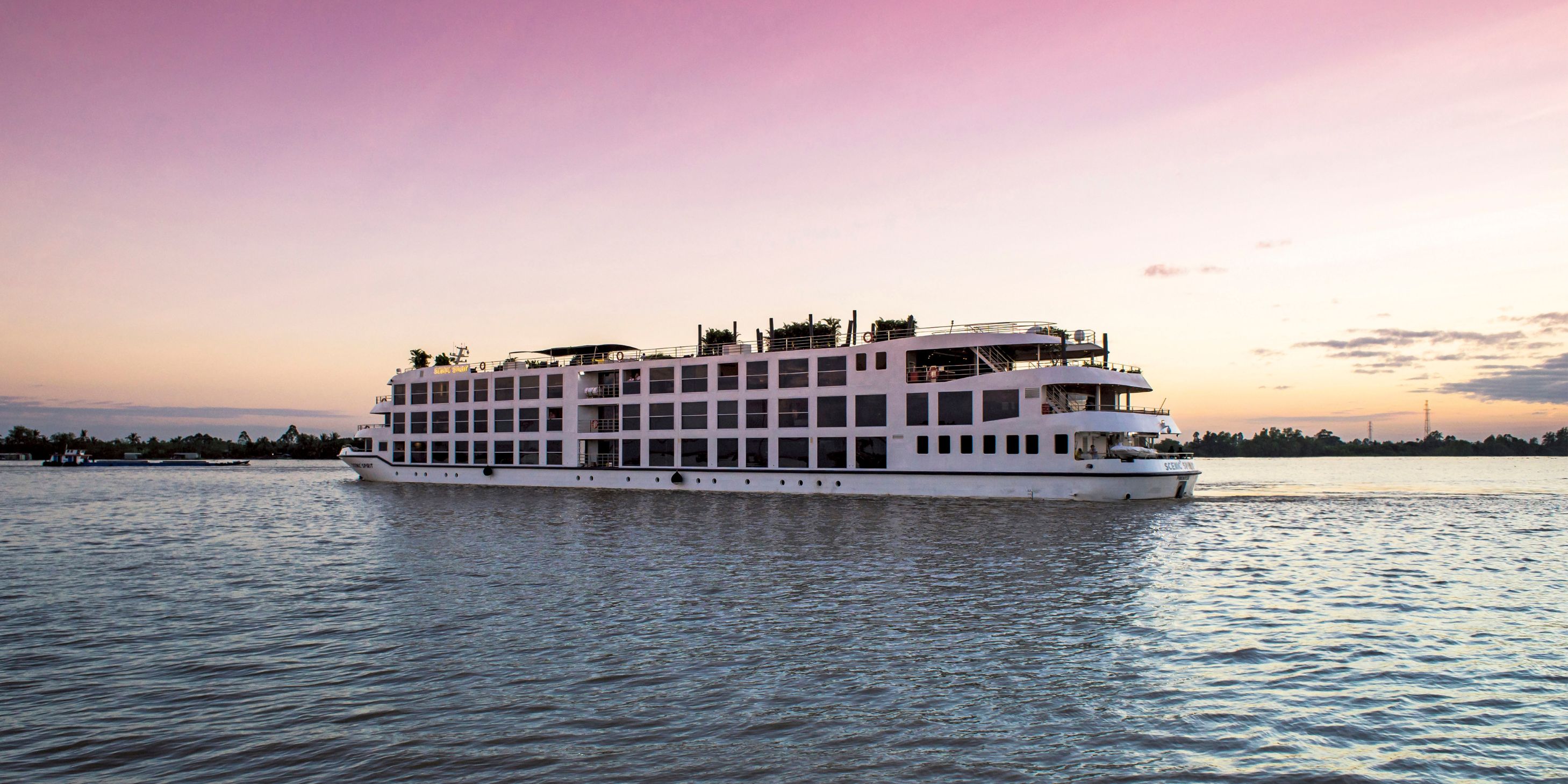 Boutique river cruise ship sailing on the Mekong river in South East Asia under a pink and orange sunset