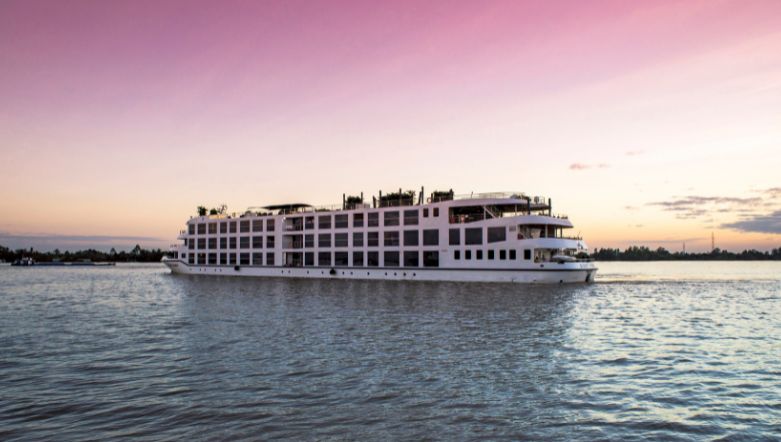 Boutique river cruise ship sailing on the Mekong river in South East Asia under a pink and orange sunset