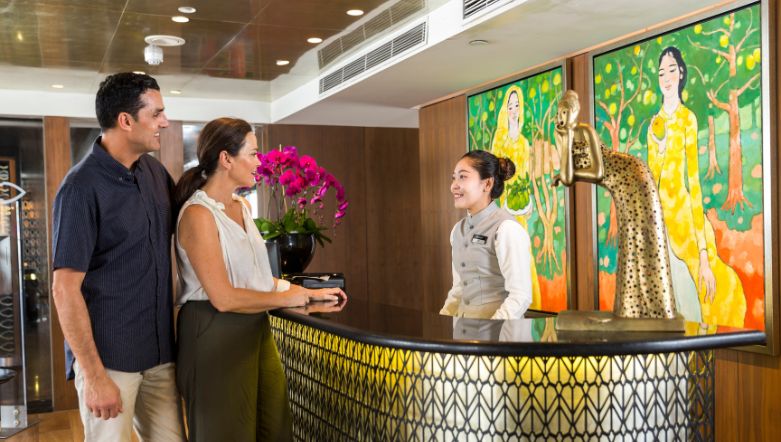 Two guests talking to a receptionist at a desk in front of vibrant artwork