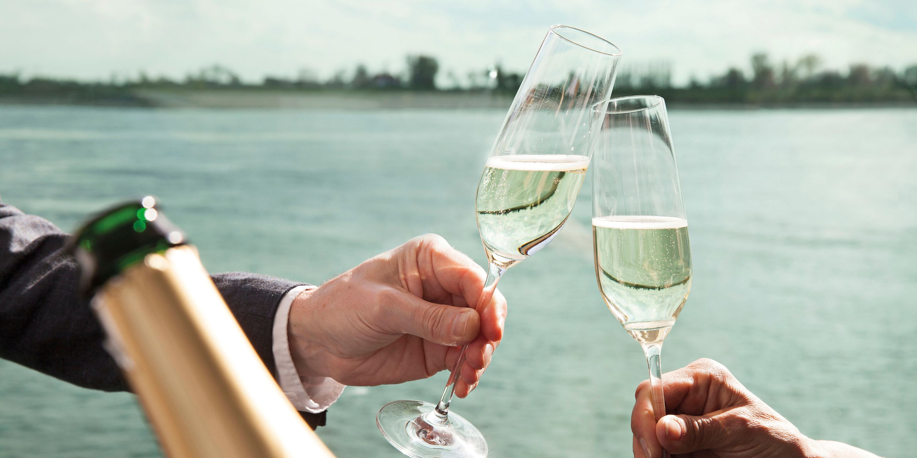 two champagne flutes clinking together in front of a river