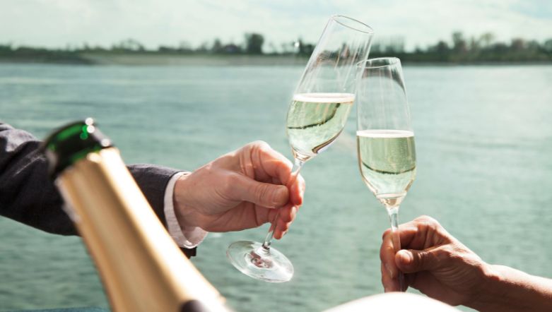 two champagne flutes clinking together in front of a river