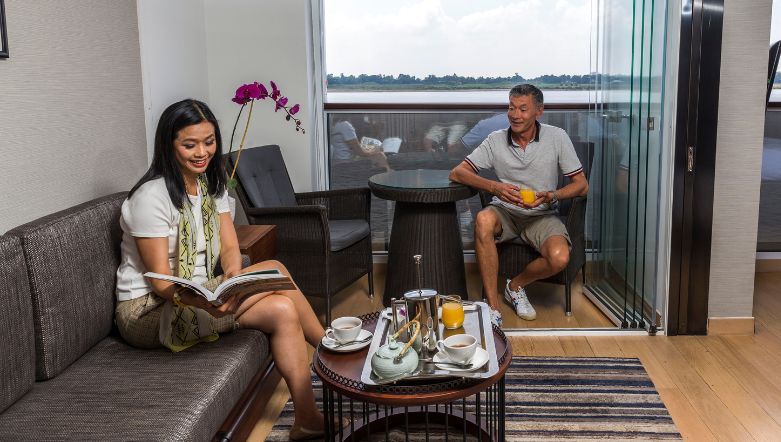 Two guests conversing with each other and looking through a magazine in their suite on board a boutique river cruise in South East Asia.