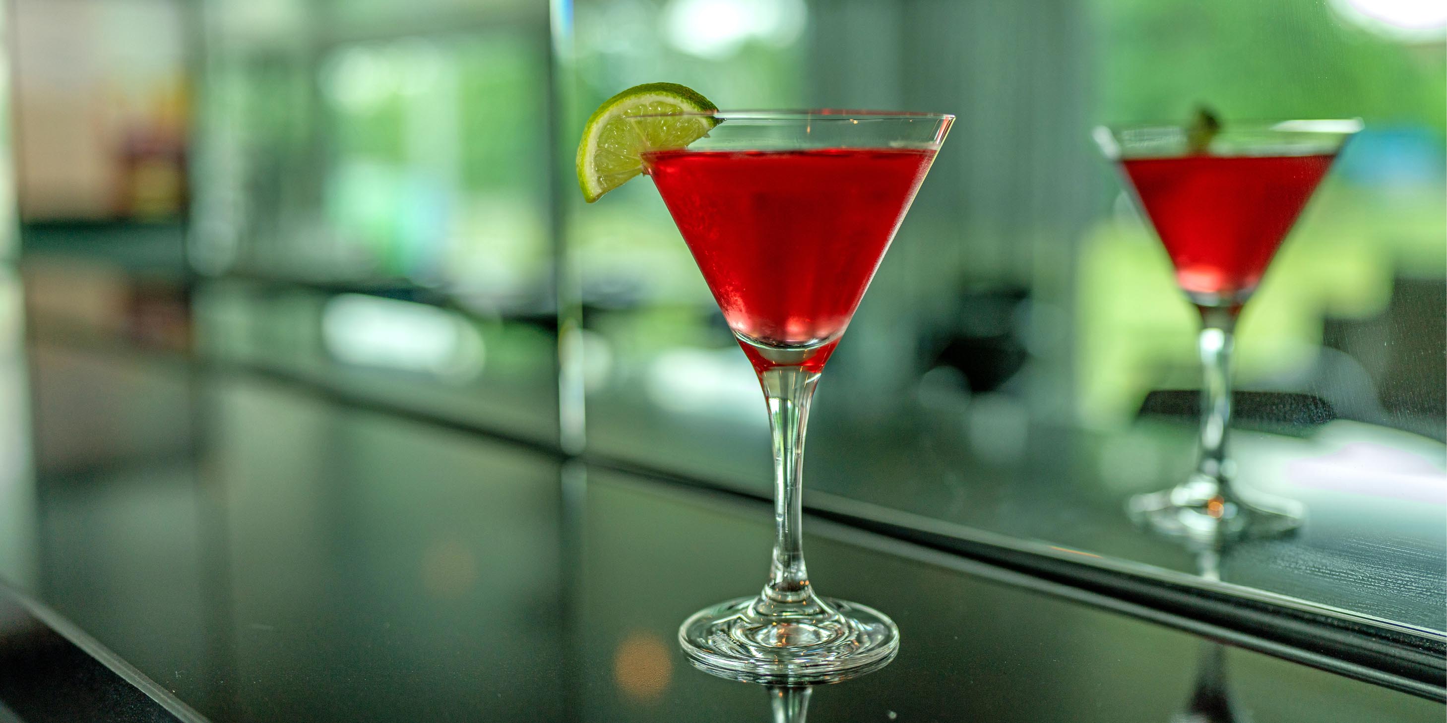 Red cocktail with a lime wedge garnish on a bar table