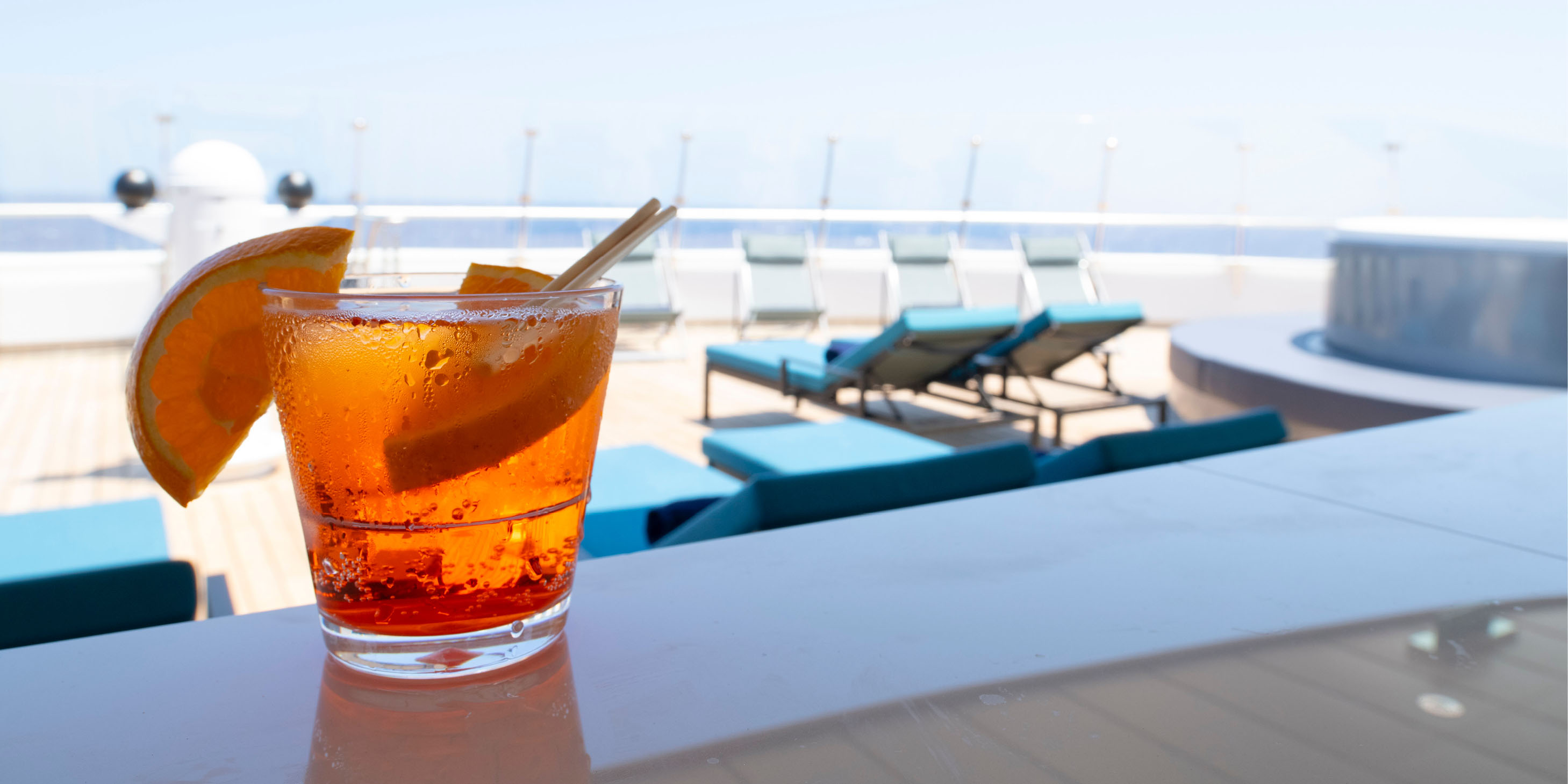 Cocktail with orange wedge garnishes on a bar bench overlooking sunlounge chairs