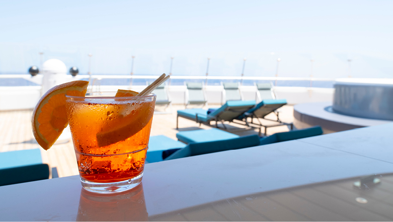 Cocktail with orange wedge garnishes on a bar bench overlooking sunlounge chairs